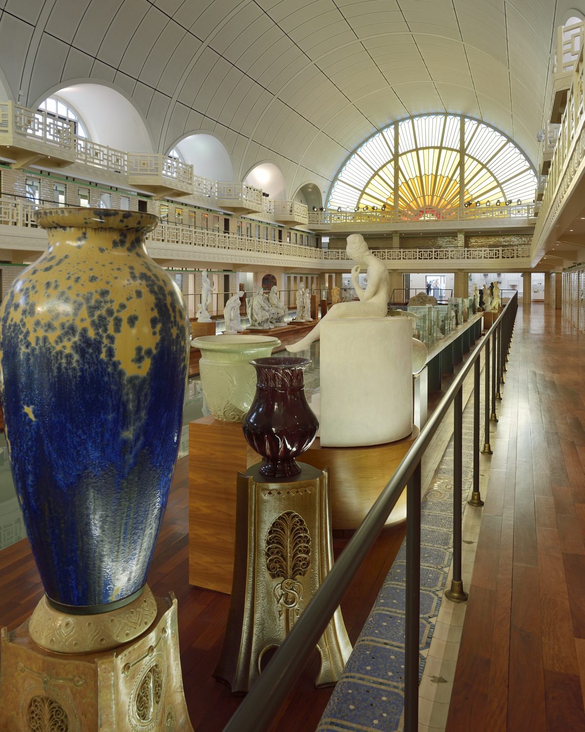 Vue de l'intérieur du bassin du musée La Piscine, installé dans une ancienne piscine Art déco, avec une grande verrière en forme de soleil coloré. Des sculptures et des céramiques sont exposées au centre, entourées de galeries et d’un plafond voûté.